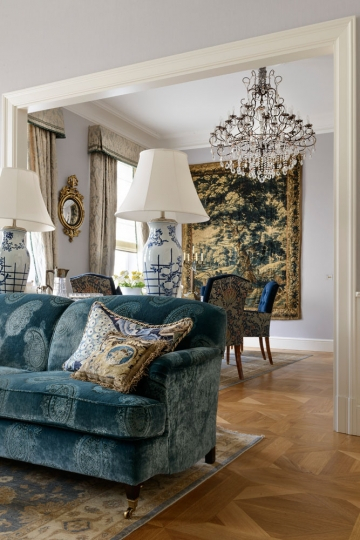 Salon w apartamencie w warszawskiej kamienicy z niebieską sofą tapicerowaną tłoczonym aksamitem, kryształowym żyrandolem i wielką tapiserią na ścianie, projekt Kanach Interiors.