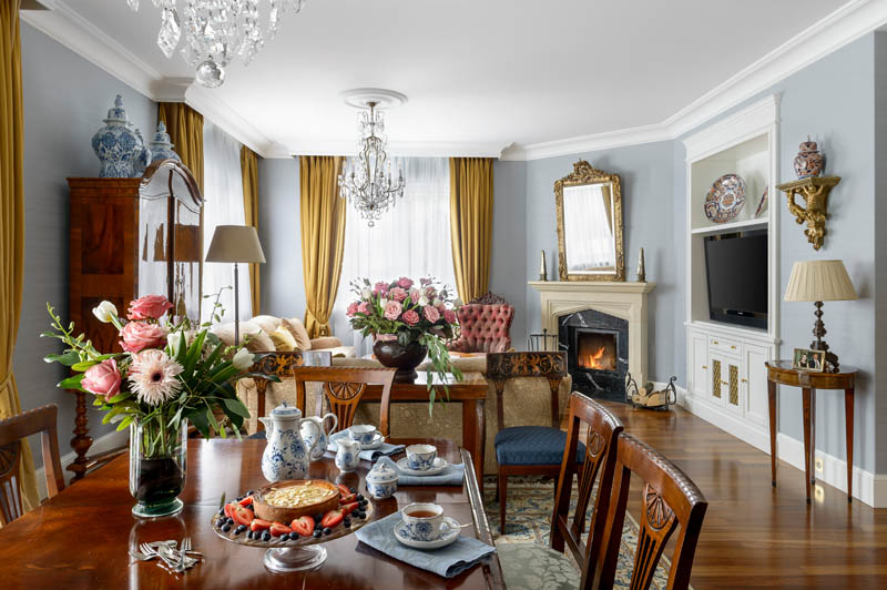 Salon w stylu klasycznym pełen antyków, kamienny portal kominkowy, kryształowy żyrandol, złocone lustro w ramie, projektowanie wnętrz ponadczasowych, projektowanie wnętrz stylowych, projektowanie wnętrz klasycznych.