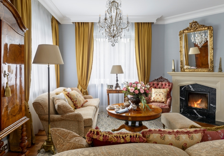 Salon w stylu klasycznym pełen antyków, kamienny portal kominkowy, kryształowy żyrandol, złocone lustro w ramie, projektowanie wnętrz ponadczasowych, projektowanie wnętrz stylowych, projektowanie wnętrz klasycznych.