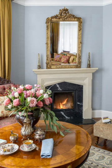 Salon w stylu klasycznym pełen antyków, kamienny portal kominkowy, intarsjowana ława do sofy, złocone lustro nad kominek, projektowanie wnętrz ponadczasowych, projektowanie wnętrz stylowych, projektowanie wnętrz klasycznych.